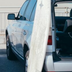 Surfboard leaning on an SUV parked by a sunny beach. Ideal for summer and travel themes.