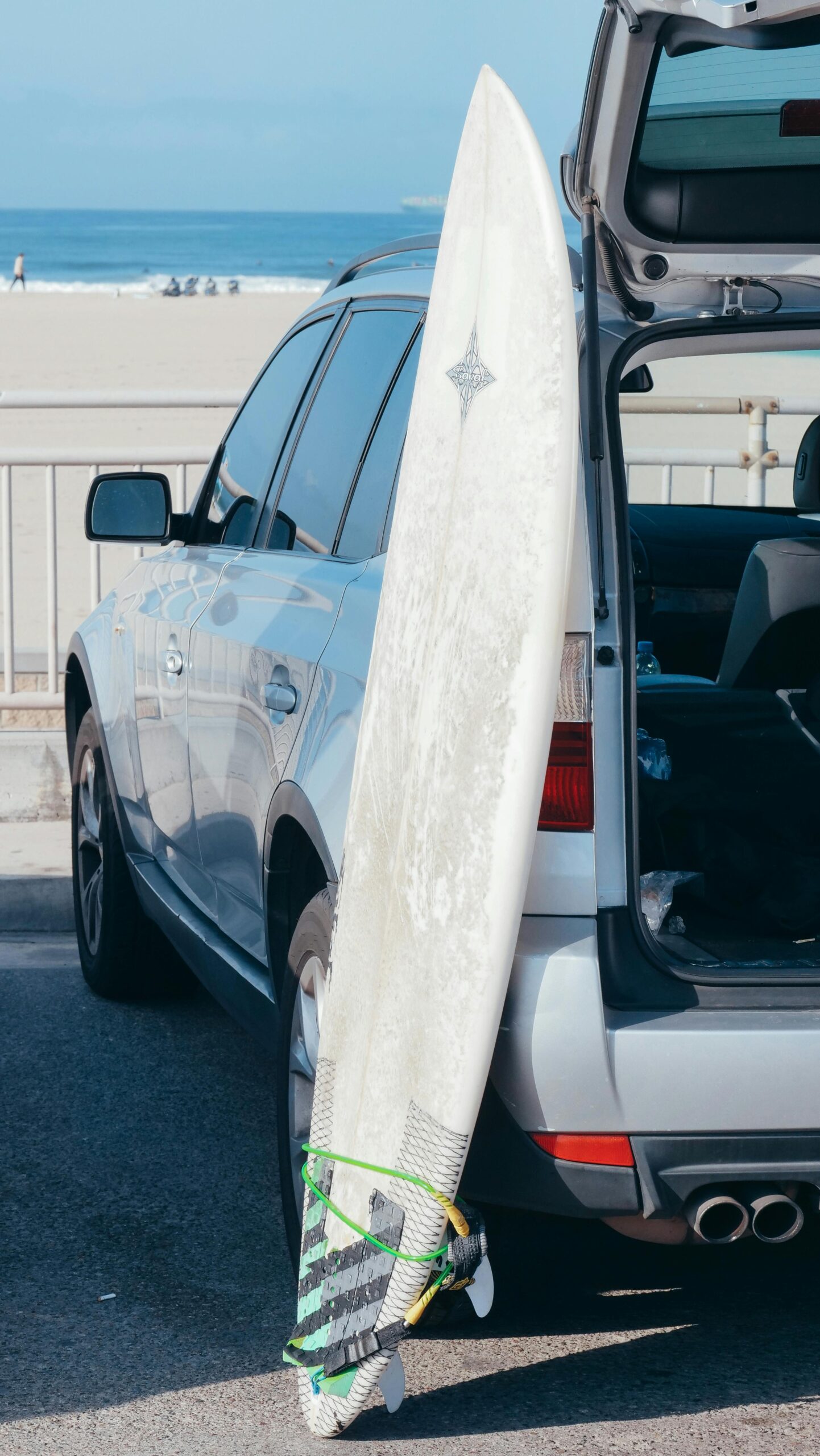 Surfboard leaning on an SUV parked by a sunny beach. Ideal for summer and travel themes.